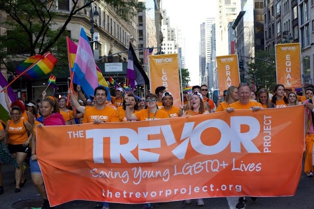 The Trevor Project team at Pride Image: The Trevor Project team holding up a sign of their logo in a Pride Parade