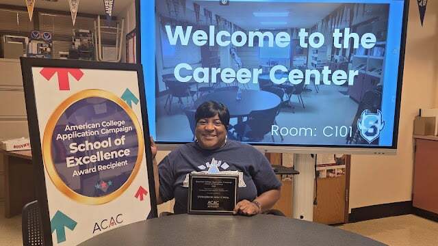 Tammy Patterson in Springbrook HS career center with ACAC School of Excellence plaque and sign
