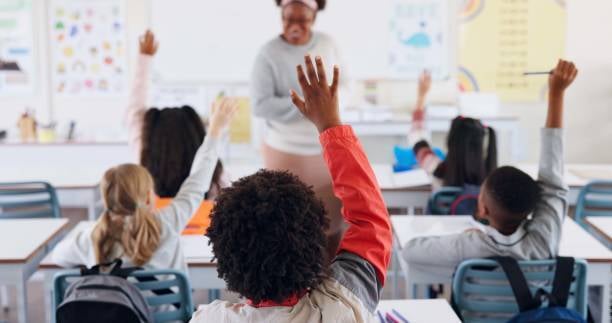 young students in class raising hands